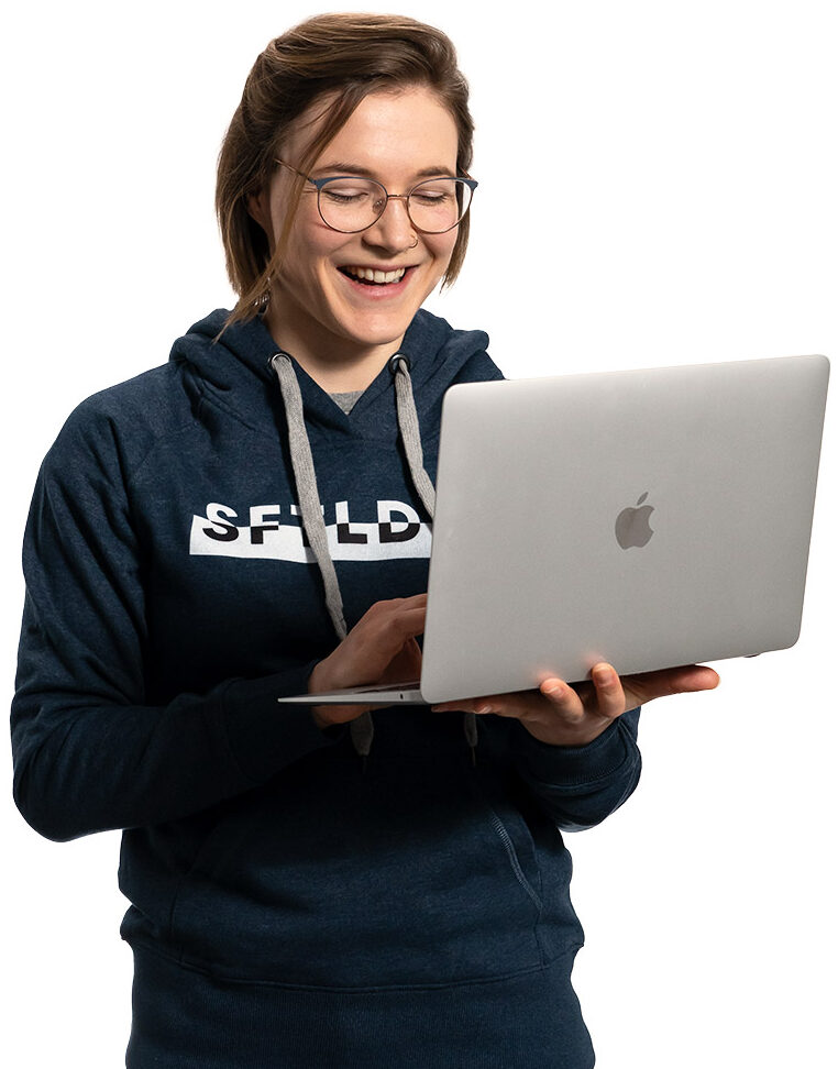 Unsere Webseitencheckerin Sharon schaut lächelnd auf ein Macbook.